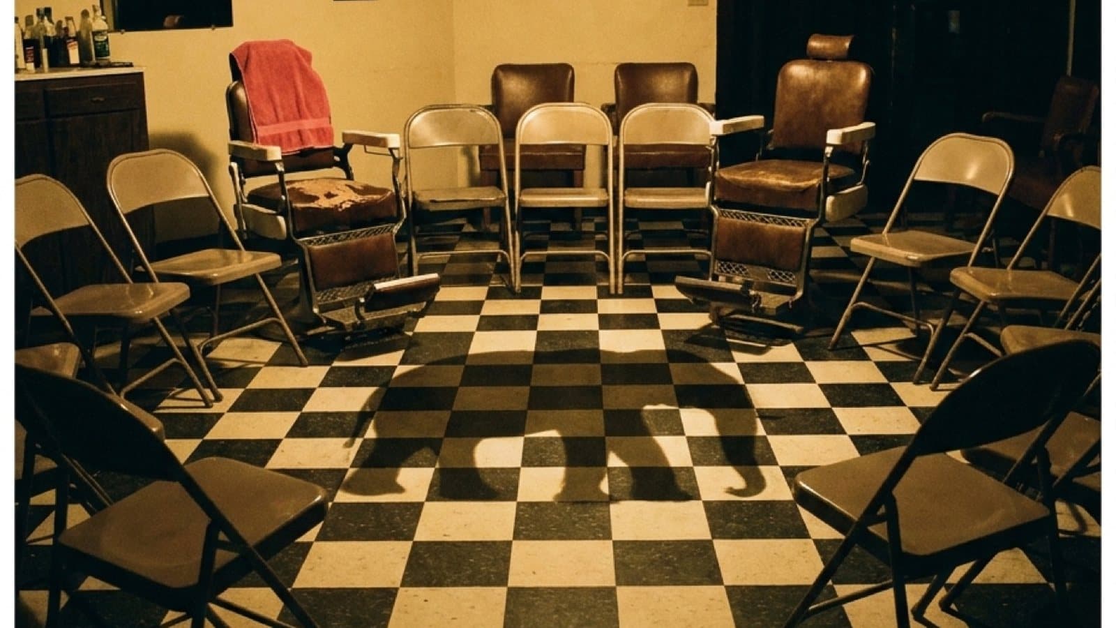 A circle of folding chairs and barber chairs on a checkered barbershop floor, set up for a recovery conversation.